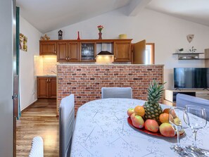 A kitchen with wooden cabinets, a brick wall, a dining table with a fruit platter, and a TV.