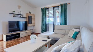 Una sala de estar moderna con una televisión de pantalla plana, un sofá, una mesa de centro y un ventanal con cortinas.