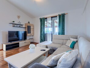 Una sala de estar moderna con una televisión de pantalla plana, un sofá, una mesa de centro y un ventanal con cortinas.