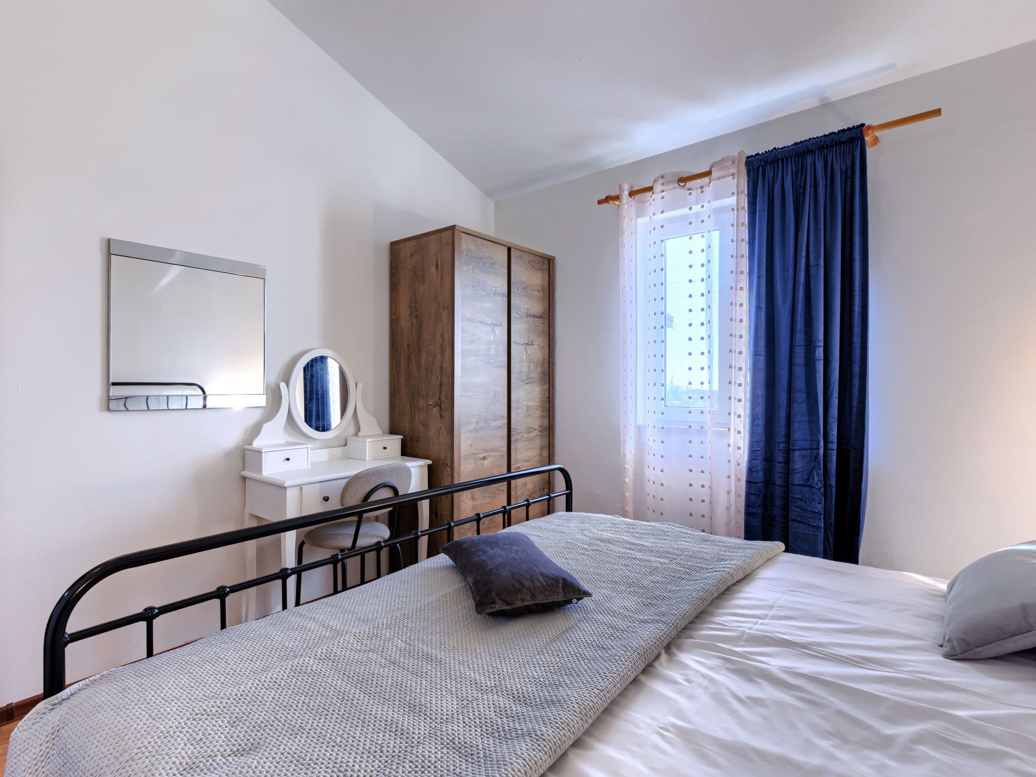 A bedroom with a bed, a dresser, a mirror, and a window with curtains.