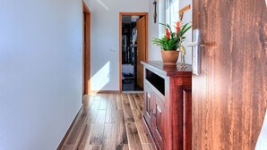 Un pasillo con suelo de madera, un mueble de madera con una planta en maceta y una puerta con ventanal.