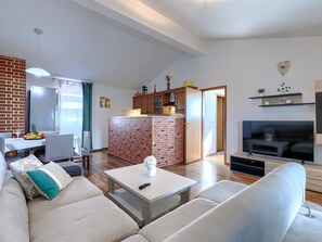 A modern living room with a sofa, a coffee table, a TV, and a kitchen area with a brick backsplash.