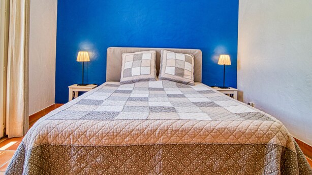 A bedroom with a blue accent wall, a quilted bedspread, two bedside lamps, and a window with curtains. - Micocoulier by Interhome (Bagnols en Forêt)