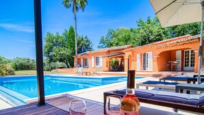 A poolside area with a wooden deck, a bottle of wine, and two glasses. - Micocoulier by Interhome (Bagnols en Forêt)