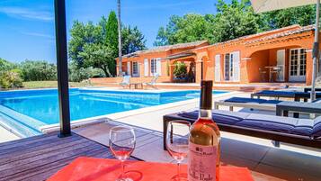 Un espace aménagé au bord de la piscine, avec une terrasse en bois, une bouteille de vin et deux verres.