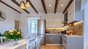 Une cuisine moderne avec des poutres en bois, un réfrigérateur en acier inoxydable et un coin repas avec des chaises blanches.