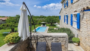 Un bâtiment en pierre avec des volets bleus, une piscine et une table avec des chaises.