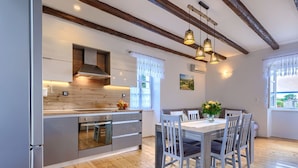 Une cuisine moderne avec des poutres en bois, un coin repas avec une table et des chaises, et une fenêtre avec des rideaux.