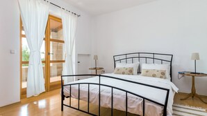 A bedroom with a metal bed frame, white bedding, a wooden floor, a small bedside table with a lamp, and a view through a glass door. - Villa Sand by Interhome (Poreč)
