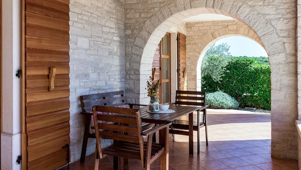 A patio with a wooden table and chairs, an archway, and a stone wall. - Villa Sand by Interhome (Poreč)
