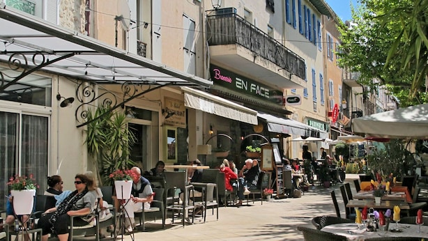 Ein Straßencafé mit Tischen und Stühlen, umgeben von Gebäuden mit Geschäften und Restaurants.