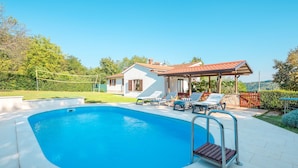 Una piscina con sillas de descanso y una pérgola, rodeada de una casa y vegetación.