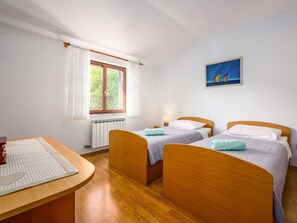 Quarto com duas camas de madeira, uma mesinha, um radiador e uma janela com cortinas.