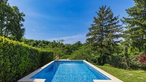 Una piscina rectangular con borde de azulejos, rodeada por un suelo de piedra y abundante vegetación.