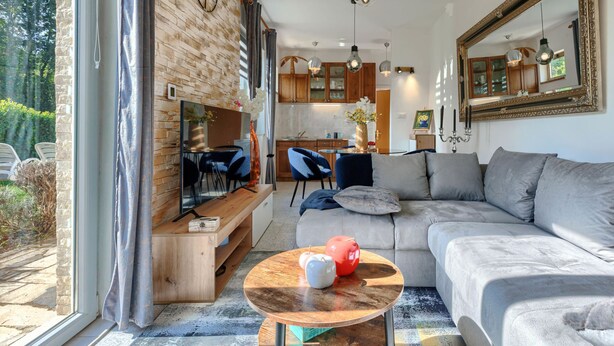 Una sala de estar moderna con un ventanal grande, un sofá, una mesita de centro y una cocina al fondo.