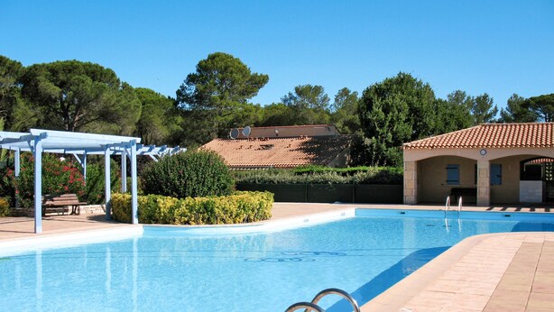 A clear blue swimming pool with a pergola and lounge chairs, surrounded by well-maintained landscaping and a building with a tiled roof. - Tiny Blue by Interhome (La Motte en Provence)