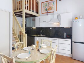 A modern kitchen with white cabinets, a black countertop, and a dining area with a glass table and chairs.