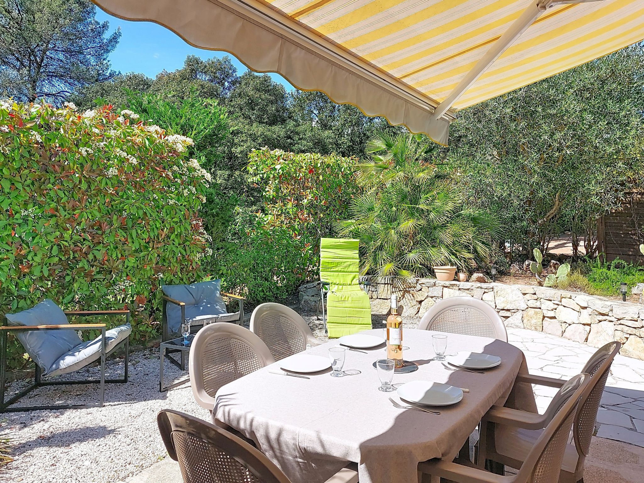 An outdoor dining area with a table set for two, surrounded by chairs, under a striped canopy.