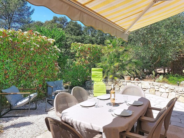An outdoor dining area with a table set for two, surrounded by chairs, under a striped canopy.