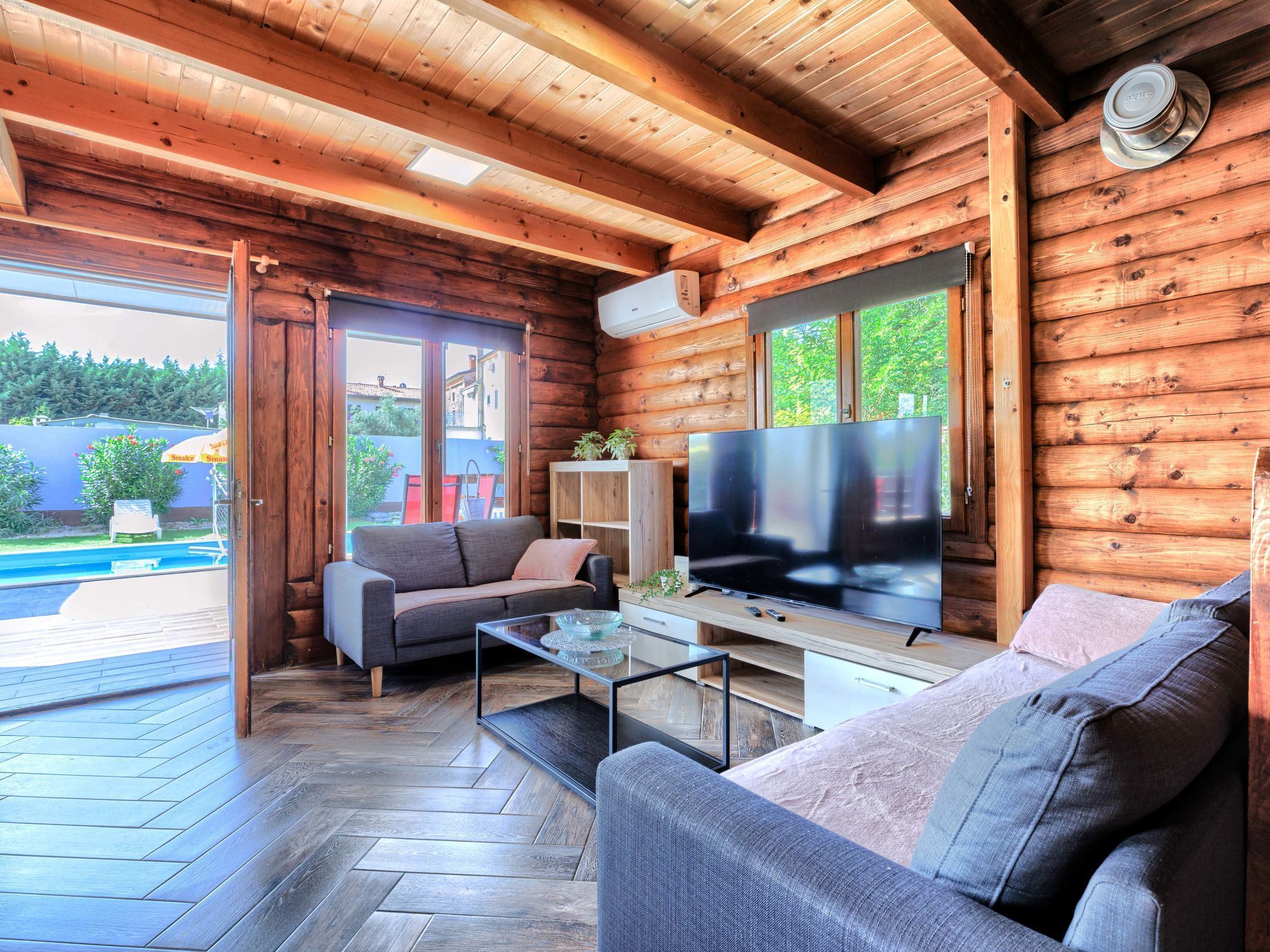 A cozy cabin interior with a wooden exterior, a large flat-screen TV, a sofa, and a glass coffee table.