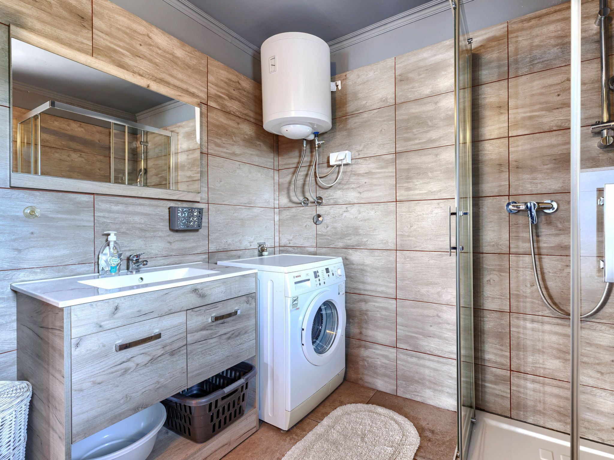 A modern bathroom with a built-in washing machine, a glass shower enclosure, and a large mirror above the sink.