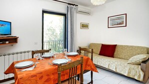 A dining area with a table set for four, a sofa, a television, and a window with a view of greenery.