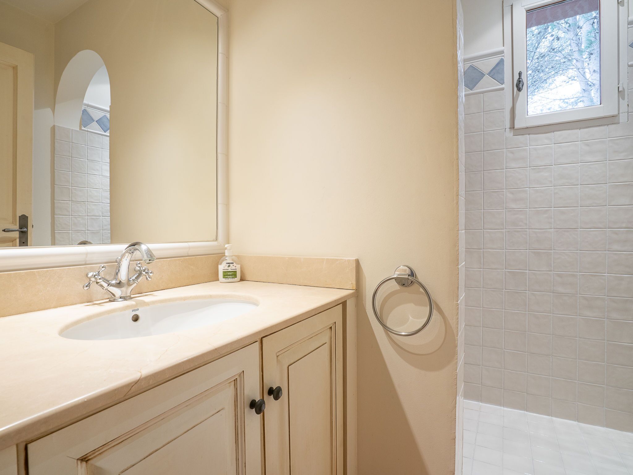 Une salle de bain avec un lavabo beige, un miroir et une fenêtre.