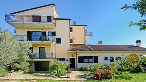 Un immeuble à plusieurs étages doté de balcons, d’un chemin en pierre et d’un jardin agrémenté de plantes en pot.