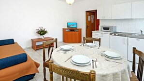 Un espace de vie compact comprenant un coin repas, une kitchenette et un téléviseur posé sur un meuble en bois.