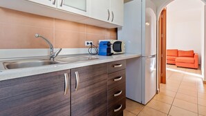 Eine moderne Küche mit Spüle aus Edelstahl, einer Mikrowelle und einem Kühlschrank. Es gibt einen Holzkorpus mit Schubladen und eine Arbeitsplatte.