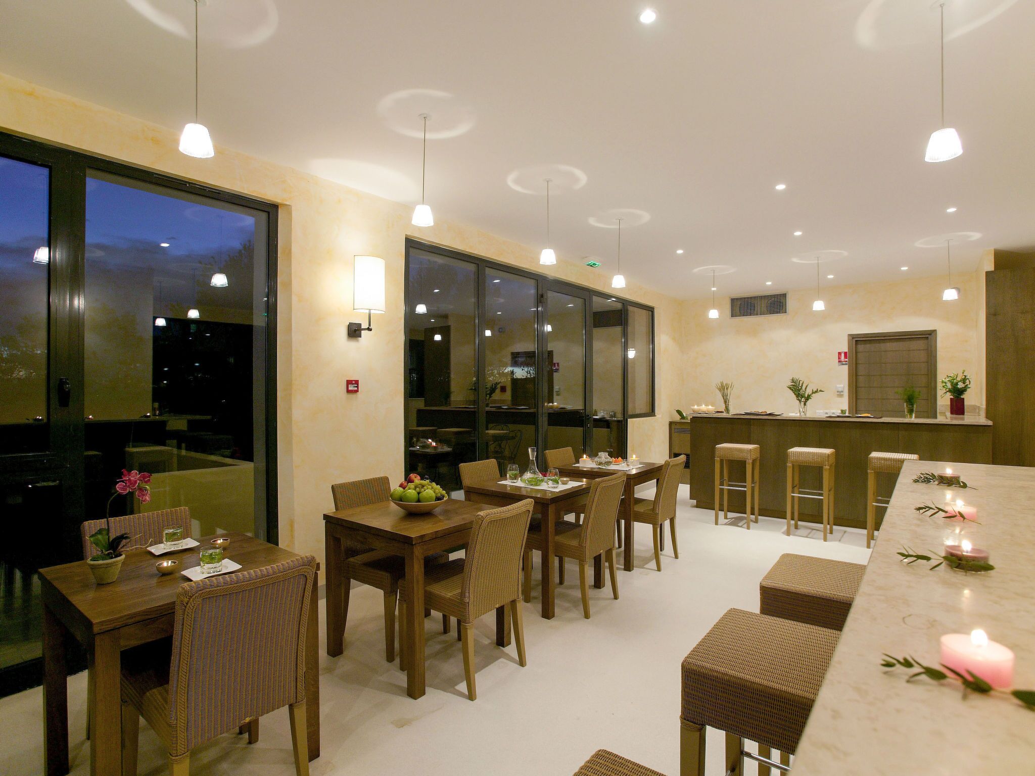 Un espace repas comprenant plusieurs tables et chaises, un comptoir de bar et de grandes fenêtres.