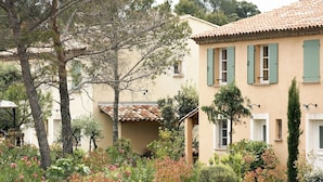 A Mediterranean-style building with a tiled roof and green shutters, surrounded by a well-maintained garden with various shrubs and flowering plants. - Le Domaine de St. Endréol Golf & Spa by Interhome (La Motte en Provence)