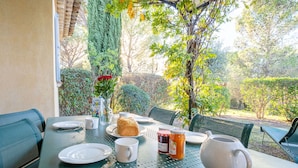 A table set for breakfast with plates, cups, a jug, and a bottle of juice, surrounded by greenery and trees. - Le Domaine de St. Endréol Golf & Spa by Interhome (La Motte en Provence)