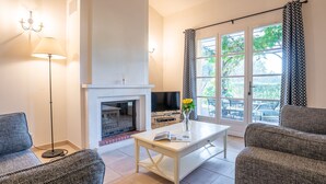 A living room with a fireplace, a television, and a window with curtains. - Le Domaine de St. Endréol Golf & Spa by Interhome (La Motte en Provence)