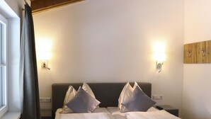 Habitación de hotel con dos camas, cada una con una almohada y una toalla enrollada. Hay luces fijadas a la pared y un panel de madera.