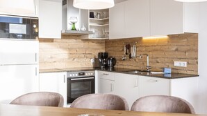 Una cocina moderna con armarios blancos, protector contra salpicaduras de madera, un horno Bosch y un comedor con una mesa y sillas de madera.