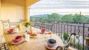 Een balkon met een ontbijttafel, met uitzicht op een schilderachtig landschap met bomen en bergen.