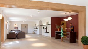 Un vaste espace de vie doté d’un plafond en bois, une cuisine à l’arrière-plan et un comptoir d’accueil où se tient une personne.