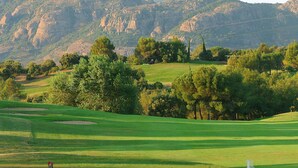 Un parcours de golf avec des collines verdoyantes, des arbres et une chaîne de montagnes en arrière-plan.