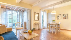 Un salon spacieux avec un canapé, une table basse sur laquelle sont disposés des fruits, un coin repas avec des chaises et une grande fenêtre avec des rideaux.