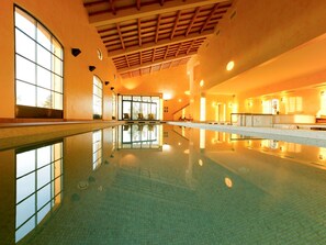 Une piscine intérieure à l’eau claire, dotée de grandes fenêtres et d’un sol carrelé.