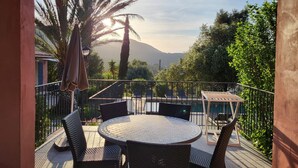 Una mesa redonda con sillas de mimbre en un balcón con vistas a una montaña y palmeras.
