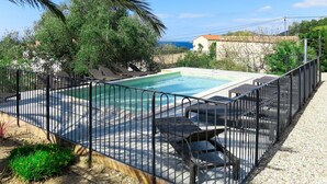 Una piscina rectangular con cerramiento metálico negro, rodeada de sillas de descanso y una zona de grava.