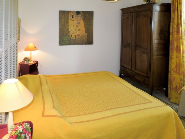 Um quarto com uma cama, um guarda-roupa de madeira, um quadro na parede e um abajur em uma mesa de cabeceira.