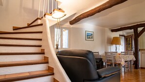 Eine Treppe mit Holzboden und weißen Wänden, ein schwarzer Ledersessel, ein Esstisch mit Blumenmuster-Tischdecke und ein Bild an der Wand.