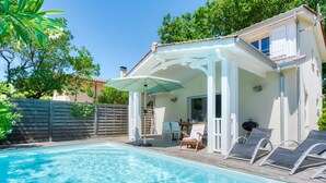 A backyard with a swimming pool, a covered patio area, and a wooden deck. - Vacation home Le Lac by Interhome (Lacanau)