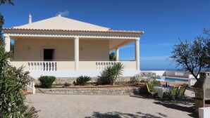 A two-story building with a tiled roof, a balcony with white balustrades, a stone wall, and a pool area with lounge chairs. - Paraíso by Interhome (Estoi)