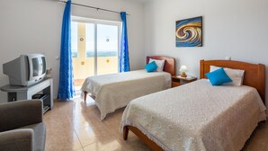 A hotel room with two beds, a TV, and a balcony with blue curtains. - Paraíso by Interhome (Estoi)