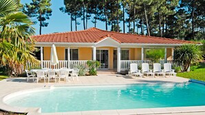 A two-story house with a swimming pool, white outdoor furniture, and a red-tiled roof.