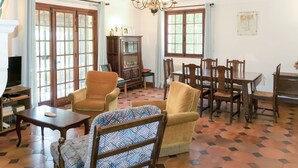 Un salon avec une cheminée, un lustre, une table à manger avec des chaises et un téléviseur.